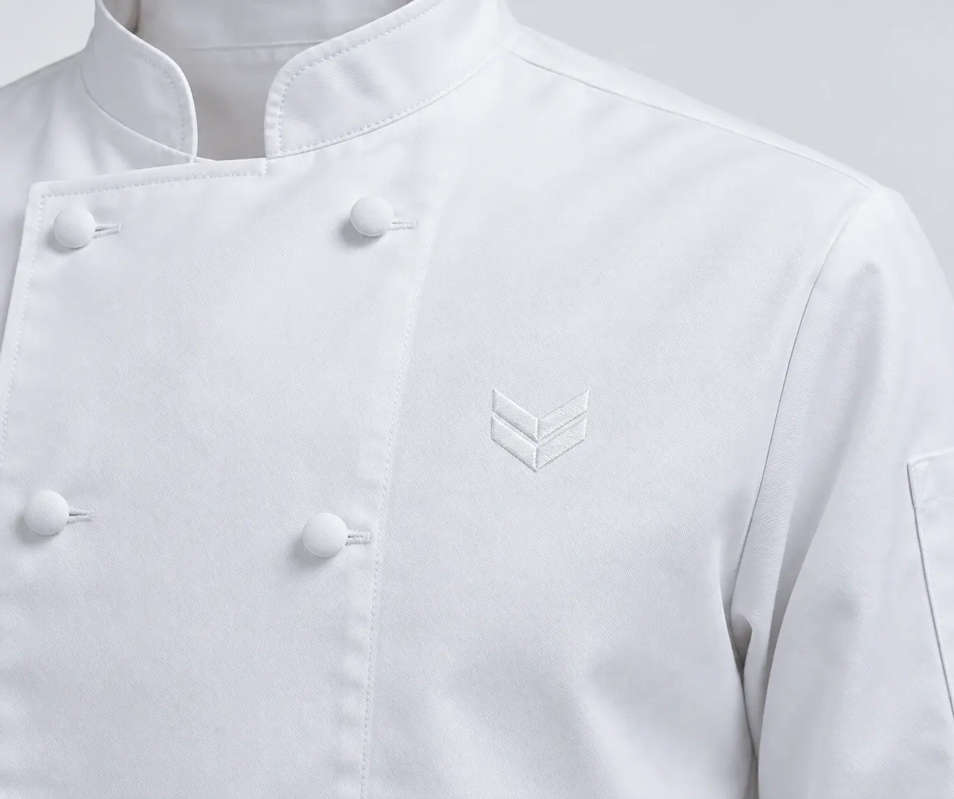 Logo chevron brodé ton sur ton sur la poitrine d'une veste de cuisine blanche.